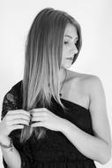 Black and white photo of the woman in dress, touching her hair, at white background