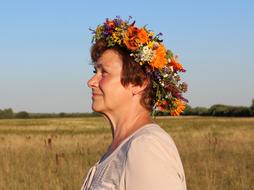 Profile portrait of the woman in colorful wreath with flowers, on the beautiful and colorful field among the trees