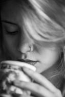 Black and white photo with the portrait of the beautiful woman with nose piercing, drinking coffee from the cup