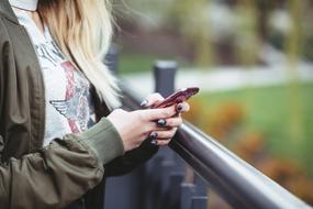 Blonde girl using smartphone near the fence, near the colorful plants