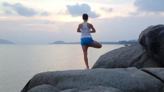 Girl standing in zen pose on stones near the sea