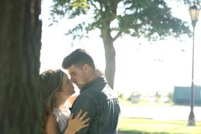 Girl and guy kissing among the plants in the park with lantern, un sunlight