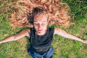 Portrait of the smiling woman, laying on the green grass, in sunlight