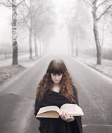 mysterious girl reading a book on a foggy road