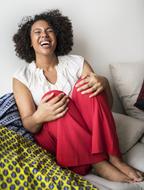 Laughing African woman with barefeet, sitting on the couch