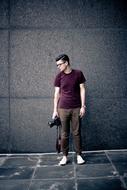 Man in glasses, with the black camera, sitting near the wall, outdoors