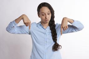 Woman in shirt, pointing down down with fingers, at white background