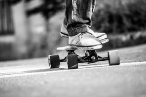 Black and white photo with the close-up of the person on the longboard, on the road, outdoors