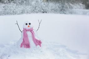 Snowman in a pink scarf in the yard in winter