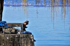 Girl sitting on the coast of Bodensee, with blue bench