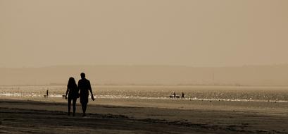 Couple of the lovers, walking on the beach, near the other people, at background with the mountains