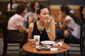 Woman with glasses eating cake and drinking coffee, near the people, in Starbucks