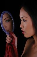 Profile portrait of the woman, looking in the mirror, at black background