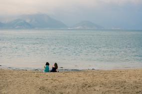 Women sitting on the sandy beach, at background with mountains, at colorful and beautiful sunset with clouds