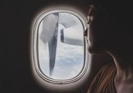 Woman looking on the blue sky with clouds, from the window of the airplane