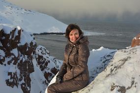 Smiling woman sitting among the snow, at the beautiful Russian North, near the water