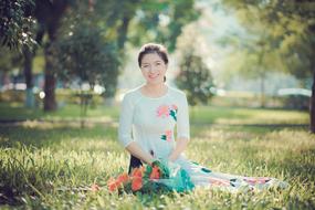 beautiful asian Girl in long dress sits on lawn in park