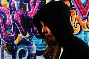 girl in a black hood against a background of colorful graffiti