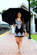 Smiling woman with black umbrella, walking on the path in water, among the green plants