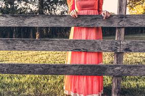 woman in long pink dress near wooden fence in countryside