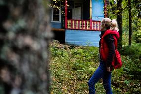 Blonde girl in red vest, near the colorful house, among the green plants of the forest