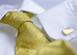 Close-up of patterned, gold tie on the white shirt with shiny cufflink