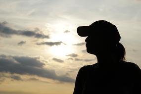 Silhouette of the woman in cap, at colorful and beautiful sunset with clouds