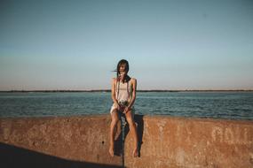 windy, a girl sits on a stone parapet by the lake