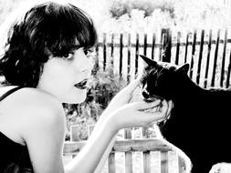 Retro, black and white photo of the woman, with the cat, near the fence and plants