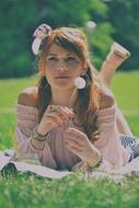 Portrait of the girl with white dandelion flower, laying on the green grass near the trees