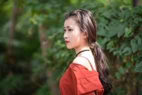 Profile portrait of the beautiful, Asian girl in red clothing, in sunlight, near the green plants