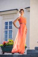 Smiling lady in the beautiful, orange dress, near the building with the colorful and beautiful flowers