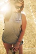 Smiling girl in sunglasses, with the skateboard, in sunlight