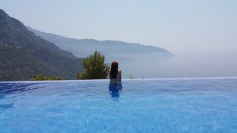 Woman sitting in the swimming pool at the beautiful view with mountains in clouds