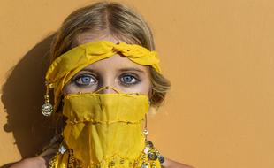 Portrait of the blonde girl in yellow clothes with accessories, in sunlight, at orange background