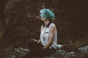 Girl with turquoise hair, sitting on the rocks, outdoors