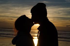 Silhouettes of the kissing couple, on the beautiful beach, at colorful and beautiful sunset