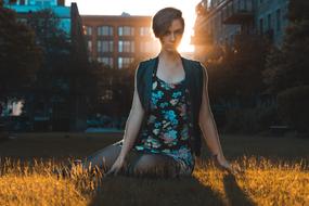 Girl sitting on the grass in sunlight, among the shadows, plants and buildings