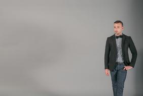 Man in suit with bow tie, posing at grey background