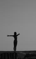 Woman with wide open hands stands back to sea