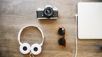 headphones and cameras next to glasses and a laptop