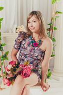 Smiling, blonde girl with colorful flowers, posing in colorful, patterned dress with flowers