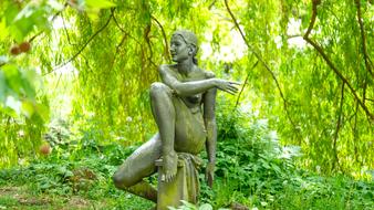 Statue of the woman, among the green plants in sunlight