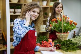 Two smiling girls in the shop with colorful flowers and stuff