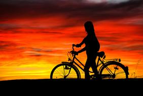 silhouette of a girl with a bicycle on the background of an orange-yellow sunset