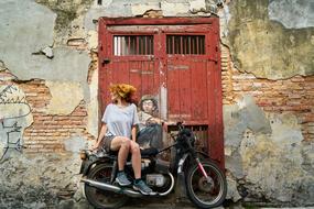 red hair girl sits on motorcycle parked at door with painted man