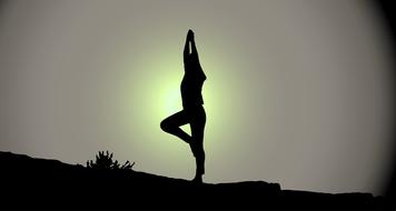 silhouettes of woman in yoga pose in dark twilight