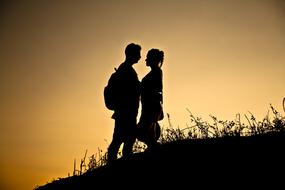 Silhouettes of the woman and man, on the hill with grass, at beautiful and colorful sunset