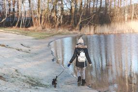 girl with small dog walks at water