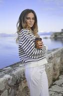 Woman with wavy hair, posing with the coffee cup, near the water